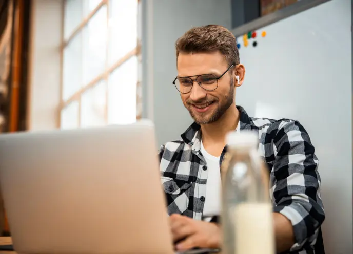 Smilende mann som jobber på laptop, og nyter en produktiv og positiv arbeidsopplevelse